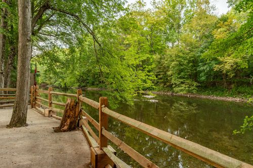 Wood split-rail fence along a paved path beside a wooded creek.