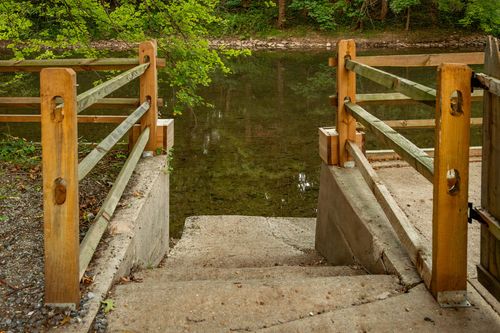 Concrete steps and a small dock leading down to a calm wooded creek.