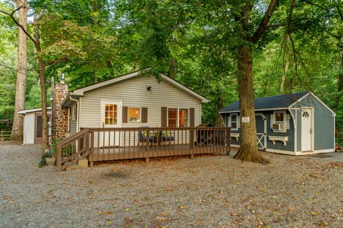 Cabin exterior with a stone chimney and gravel driveway tucked into a wooded lot.