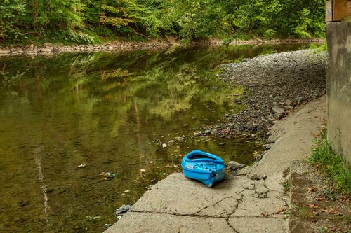 Blue kayak resting on a concrete boat ramp beside a calm, tree-lined creek.
