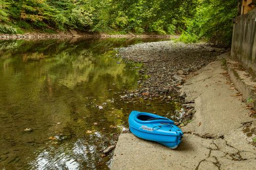 Blue kayak pulled onto a stone creek bank surrounded by wooded shoreline.