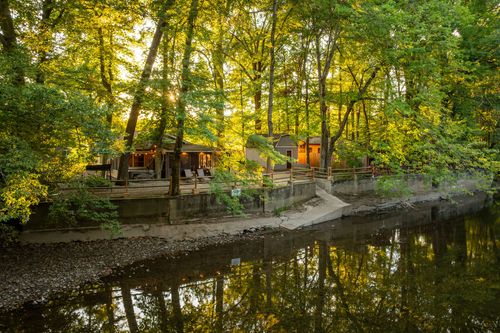 Cabin viewed across the creek at golden hour, with a deck and retaining wall along the water.