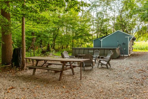 Gravel fire pit area with a picnic table, adirondack chairs and an above-ground pool nearby.