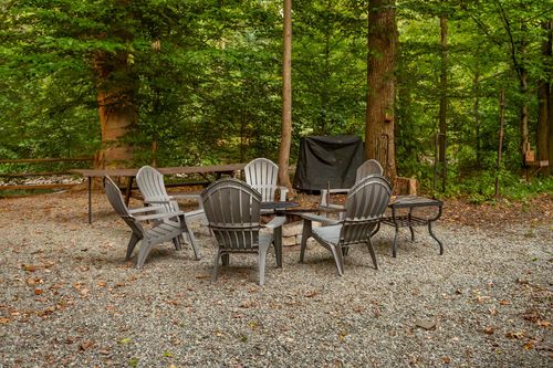 Fire pit seating area with six chairs, a wrought iron side table and a covered pool in the background.