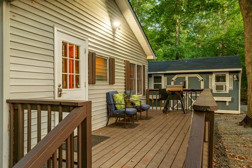 Deck seating area with cushioned patio chairs, a wood railing and a red front door.