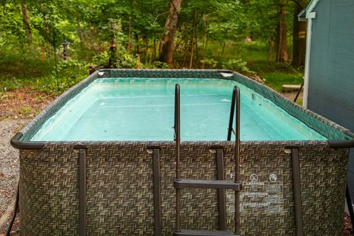 Above-ground pool entry steps and ladder, water reflecting the surrounding trees.