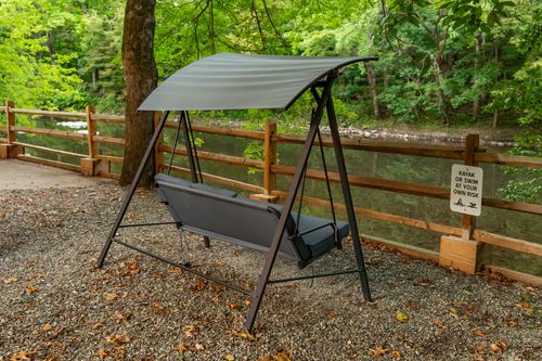 Covered porch swing overlooking a wood-fenced creek path, with a kayak-at-own-risk sign nearby.
