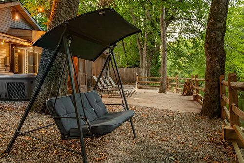 Canopy swing bench in a gravel yard, with string lights and the cabin glowing in the background.