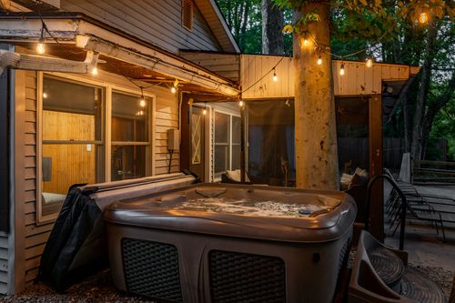 Covered hot tub beside a screened porch, wrapped in string lights strung through the trees.
