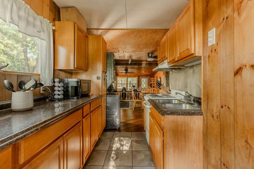 Narrow galley kitchen with warm wood cabinets, dark countertops and knotty pine paneling.