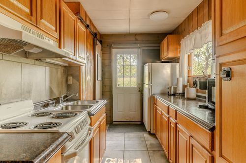 Rustic kitchen with knotty pine walls, wood cabinetry and a glass back door leading outside.