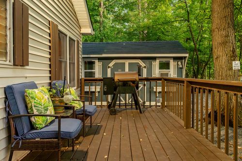 Covered deck with blue cushioned chairs, throw pillows and a view of a nearby storage shed.