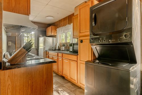 Kitchen with wood cabinetry and a stacked black washer and dryer built into the cabinets.