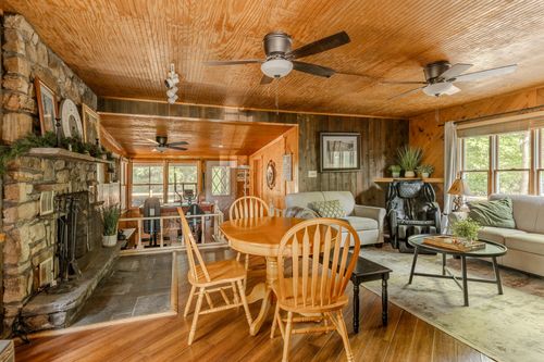 Knotty-pine living and dining area with a stone fireplace, ceiling fans and a round oak table.