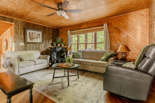 Cozy wood-paneled living room with a ceiling fan, leather recliner and cream sofa.