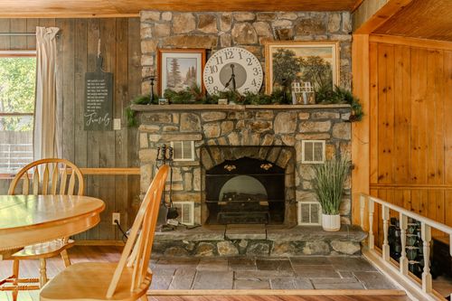 Stone fireplace with a rustic wood mantel displaying a clock and framed nature prints.