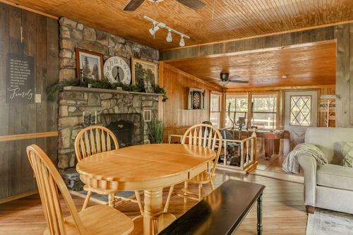 Dining nook beside a stone fireplace, with a wood table, ladder-back chairs and bench seating.