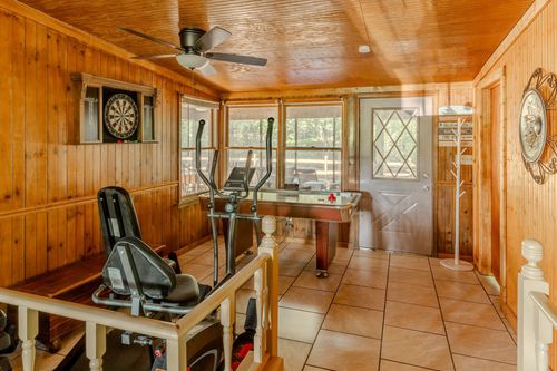 Wood-paneled game room with a dartboard, elliptical machine and air hockey table.