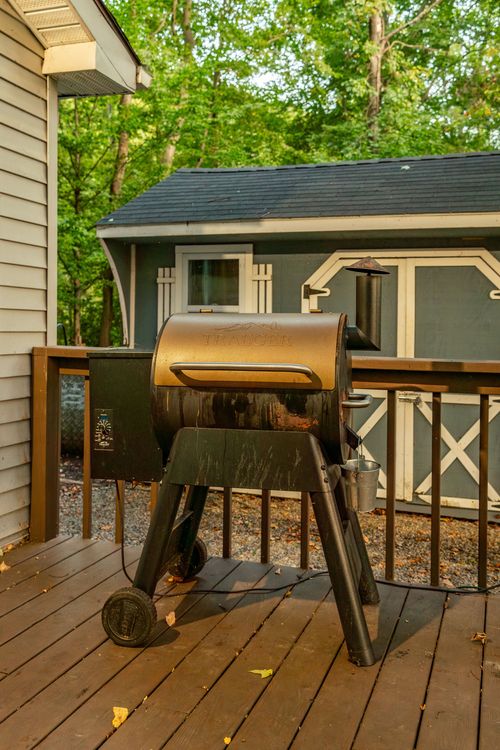 Close-up of a wood pellet grill set up on a wood deck with a storage shed in the background.