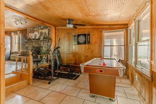 Cabin game room with a stone fireplace, elliptical machine and air hockey table.