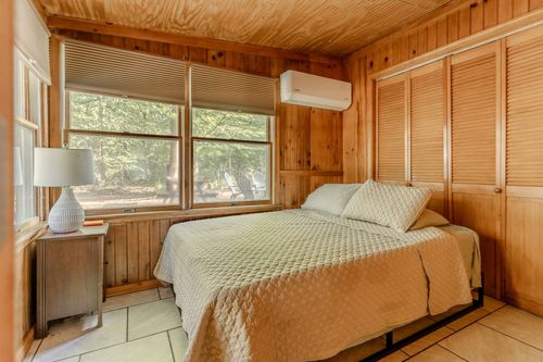 Cozy knotty-pine bedroom with louvered closet doors and a mounted air conditioner.