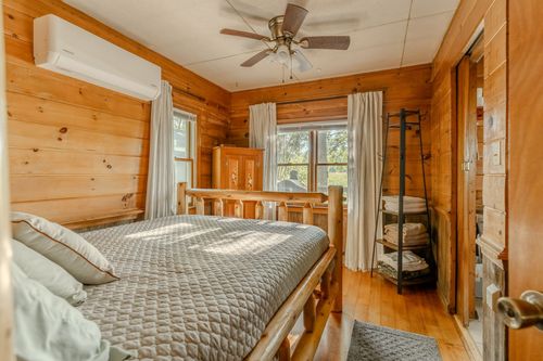 Bedroom with a rustic log bed frame, wood armoire and open towel shelving.