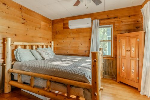 Rustic bedroom with a log bed frame, ceiling fan and knotty pine walls throughout.