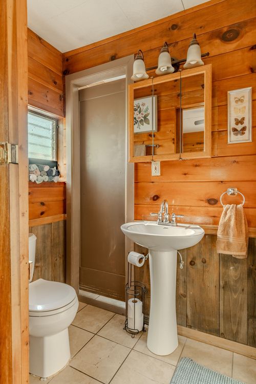 Bathroom with a pedestal sink, wood medicine cabinet and a matching toilet on tile flooring.