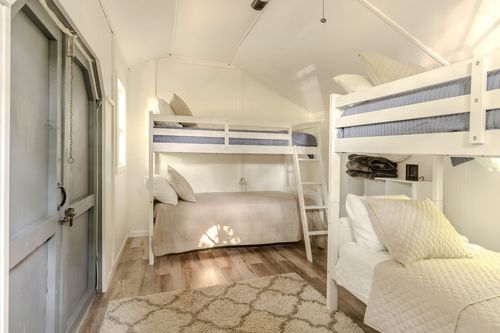 Bunkroom with two white bunk beds, a shag rug and wood floors under a vaulted ceiling.
