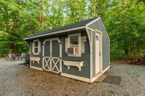 Blue storage shed with white trim, a wood door and a window air conditioner unit.