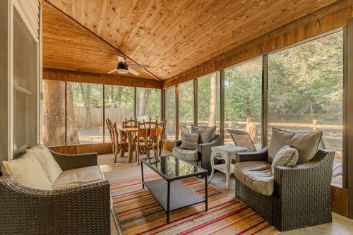 Screened porch with a wood-plank ceiling, wicker seating and a round dining table among the trees.