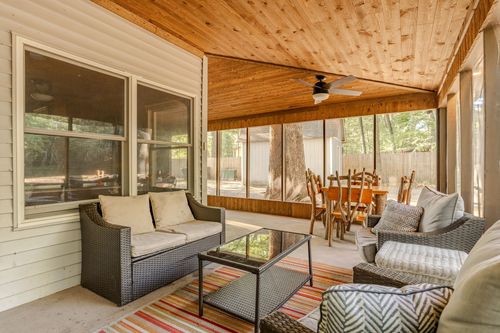 Screened porch with wicker sofas, a striped rug and a ceiling fan overlooking a wooded backyard.