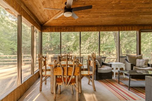 Screened porch dining area with rustic log-style chairs and a wood-plank vaulted ceiling.