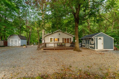 Cabin nestled among trees with two matching storage sheds and a gravel driveway.