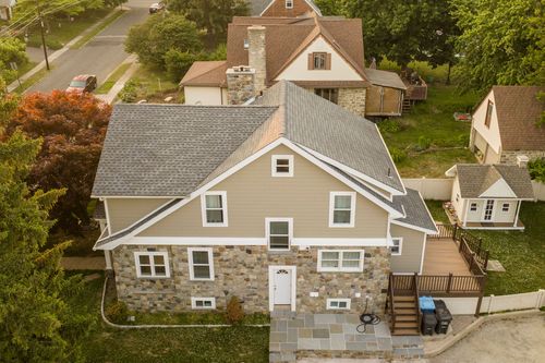 Aerial view of a stone-and-shingle craftsman home with a rear deck and neighboring houses.