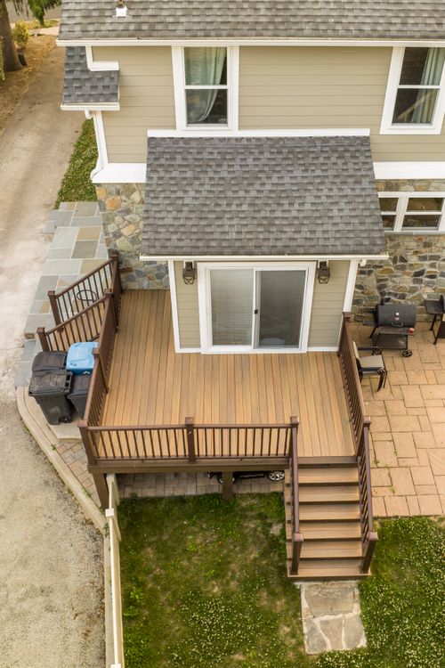 Aerial view of a sunroom addition with sliding glass door opening onto a wood deck and stone patio