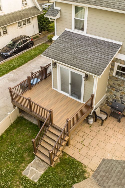 Aerial view of a multi-level deck with stair access down to a stone paver patio and grill