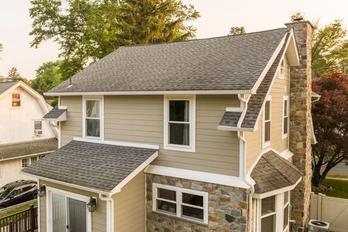 Aerial oblique view of a tan siding home with stone chimney and gray shingle roof