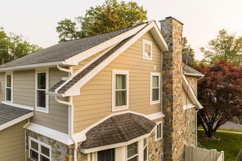 Close aerial view of a stone chimney and gabled roofline on a tan siding home
