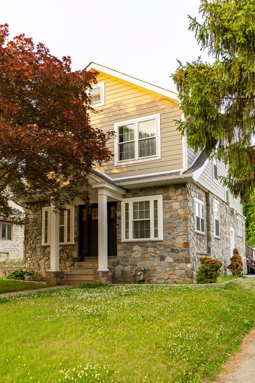 Two-story home with stone-clad first floor, covered entry porch and manicured front lawn