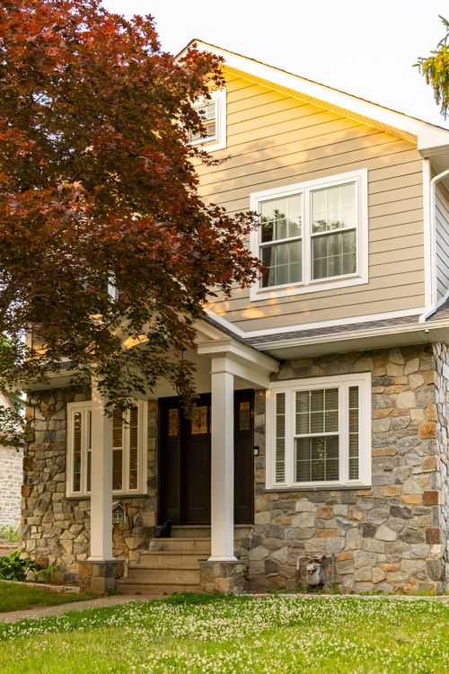 Stone-and-siding home entrance with white columned porch and dark front door
