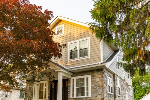 Front corner view of a two-story home with tan siding, stone base and covered entry