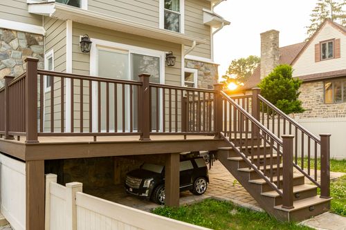Wood deck with staircase leading down to a driveway parking area at sunset