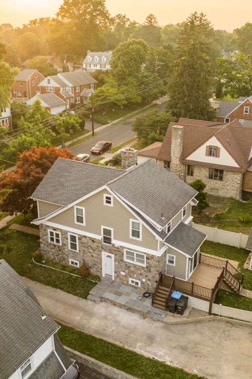 Aerial view of a craftsman-style home in a leafy neighborhood, glowing in golden evening light.