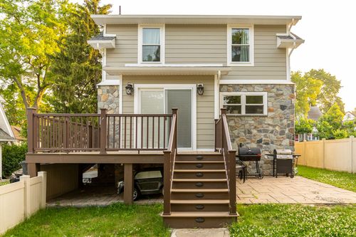 Rear of a home with new deck, sliding glass door and staircase down to a stone patio