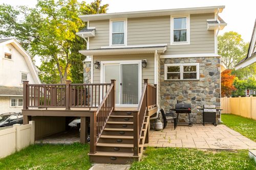 Two-story addition with stone base and new wood deck featuring a grill and patio furniture