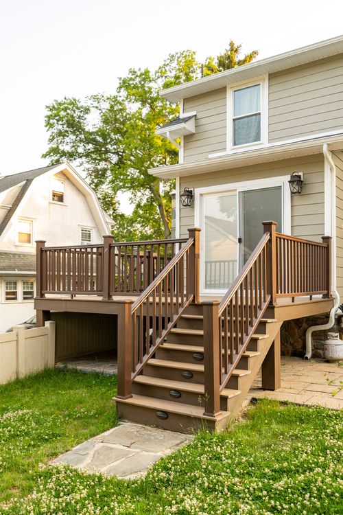 New wood deck with staircase down to a stone patio behind a tan siding home
