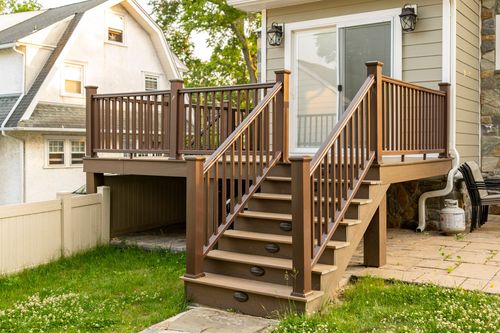 New wood deck with dark railings and staircase leading down to a stone paver walkway