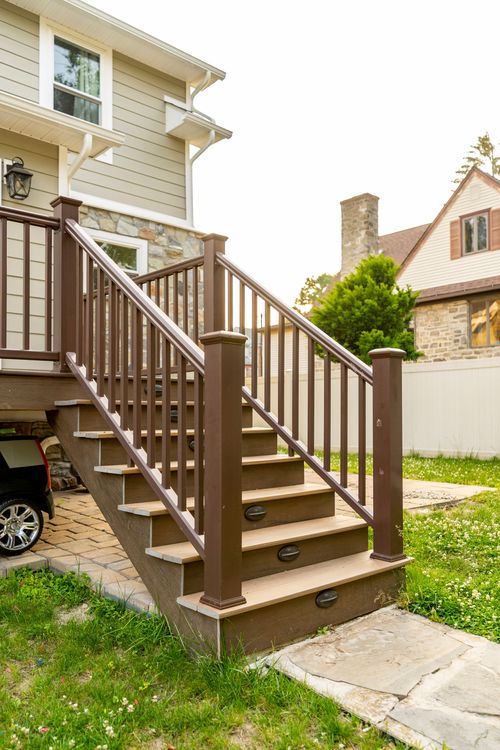 Deck staircase with dark wood railings next to a stone chimney and neighboring house