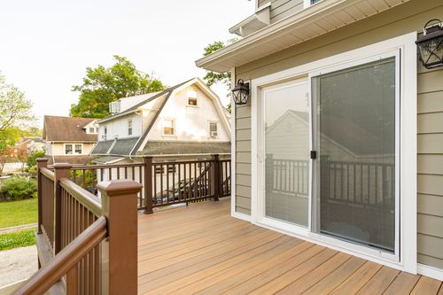 Wood deck corner view with sliding glass door and railings overlooking neighboring rooftops